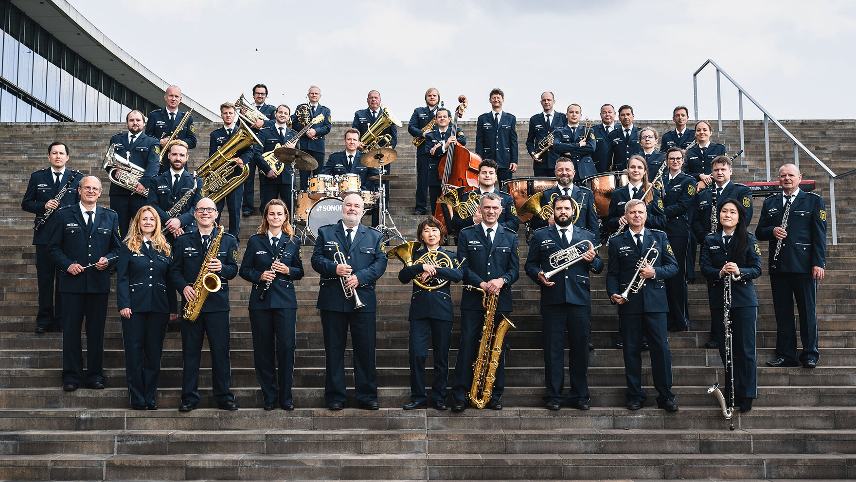 Die Musikerinnen und Musiker des Polizeiorchesters der Polizei Sachsen haben sich zu einem Gruppenfoto versammelt. Sie tragen ihre Uniformen und halten ihre Instrumente in der Hand.