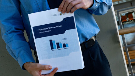 Die Polizeiliche Kriminalstatistik 2024 (PKS) vorgestellt: Ein Polizist in Uniform hält ein Dokument mit Statistiken in der Hand. Das Dokument ist beschriftet mit: »Polizeiliche Kriminalstatistik – Jahresüberblick 2024«.