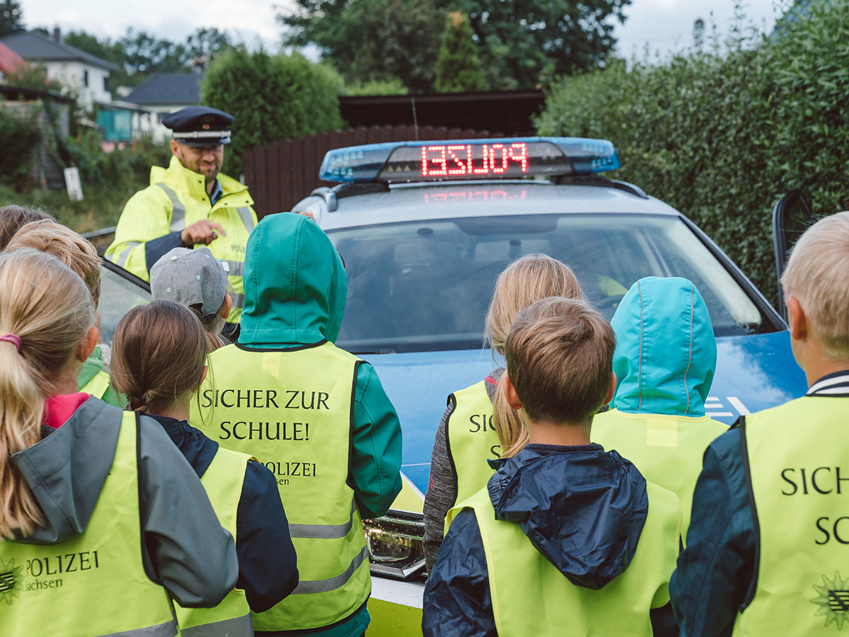 Schulkinder vor einem Polizeifahrzeug.