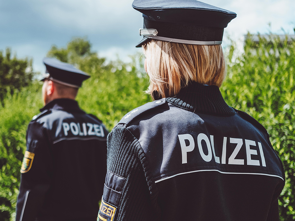 Zwei Polizisten mit blauer Uniform vor einem Feld 