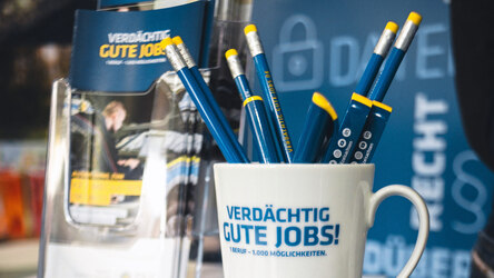 Detailaufnahme einer Berufsmesse der Polizei Sachsen: Eine Tasse sowie Stifte und Flyer mit der Aufschrift der Karrierekampagne »Verdächtig gute Jobs«. Auch die Personalabteilung des Polizeipräsidiums für Service und IT (PPSI) ist auf vielen Jobmessen.