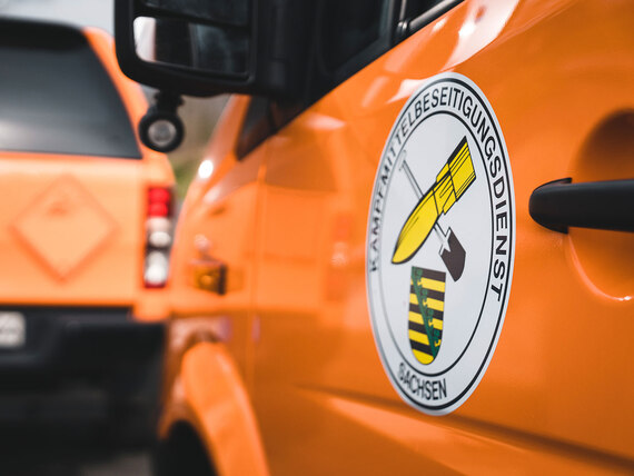 Auf einem orangenen Einsatzfahrzeug des Polizeiverwaltungsamtes ist das Logo des Kampfmittelbeseitigungsdienstes (KMBD) zu sehen.
